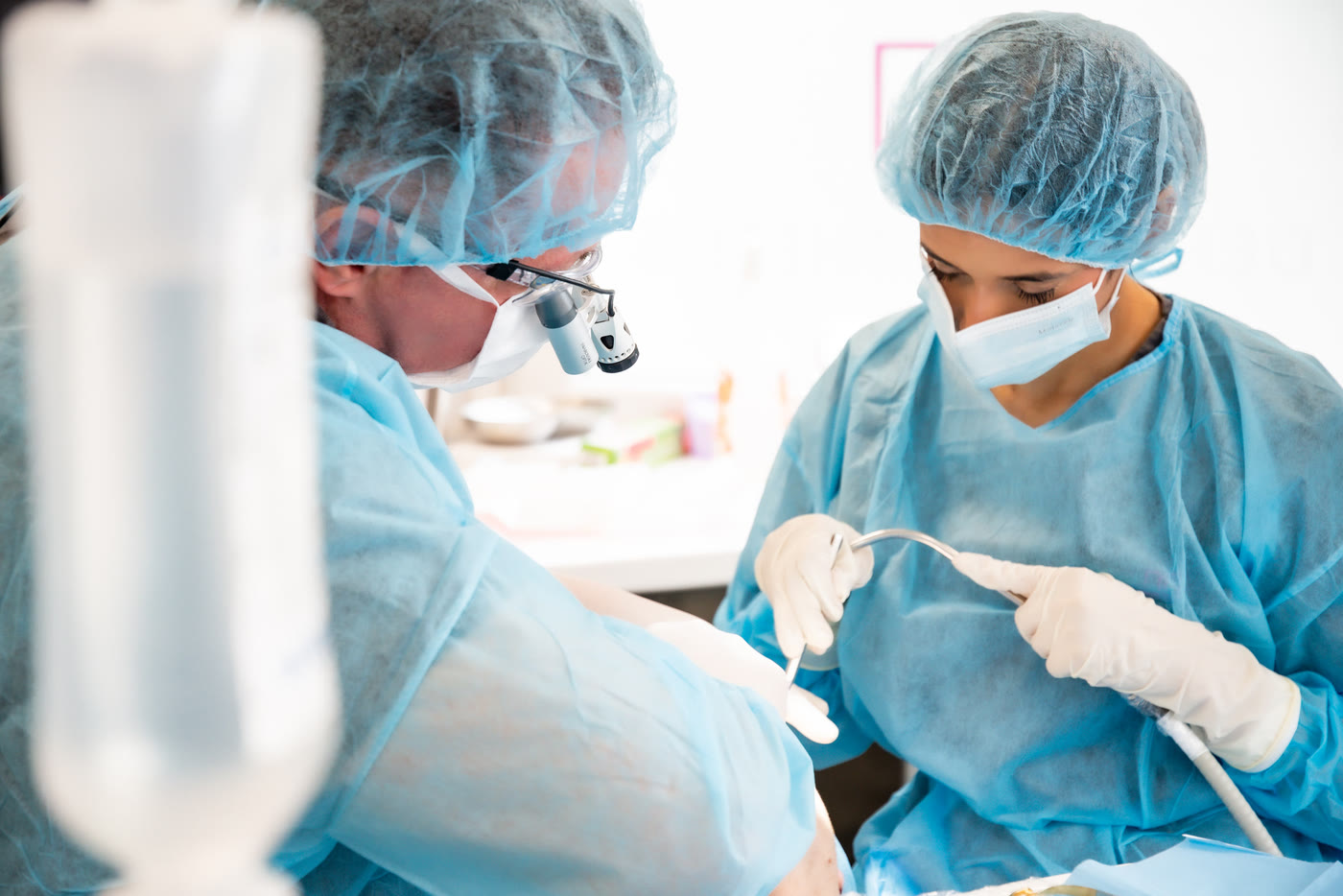 Implant treatment: dentist wearing magnifying loupes with an assistant in the sterile surgery room